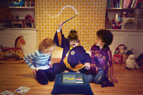 three children surrounding a tablet and the center child waving a wand