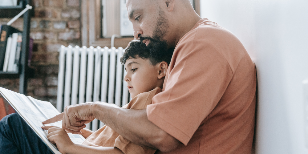 Father and son sitting together and pointing at the page of a picture book.