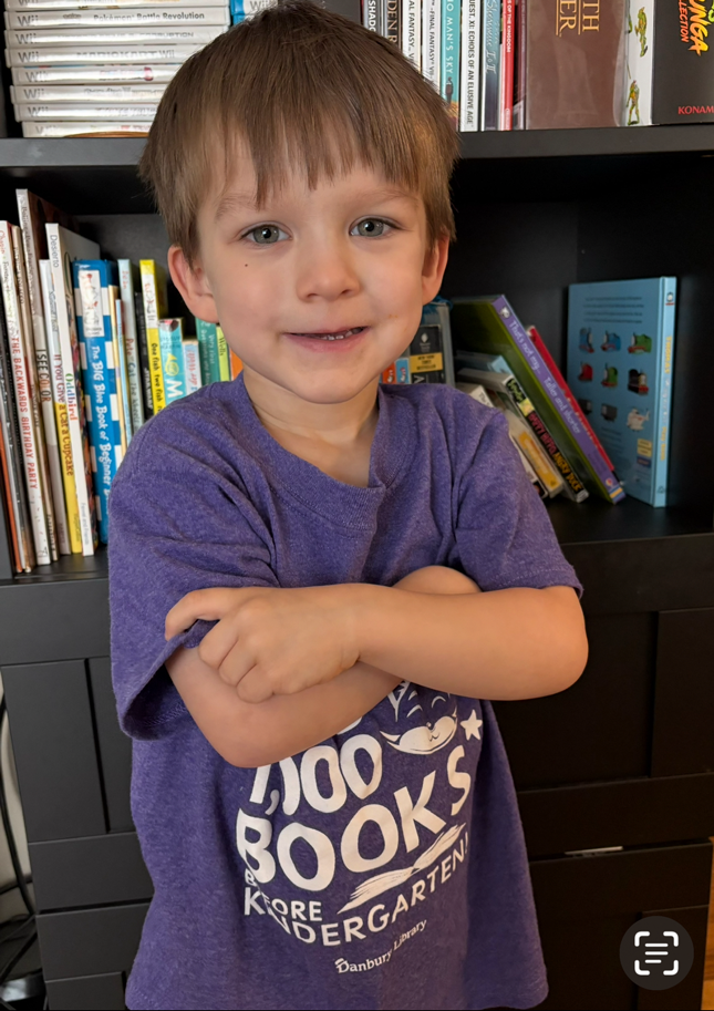 Photo of child wearing 1000 books before kindergarten shirt in front of bookcase