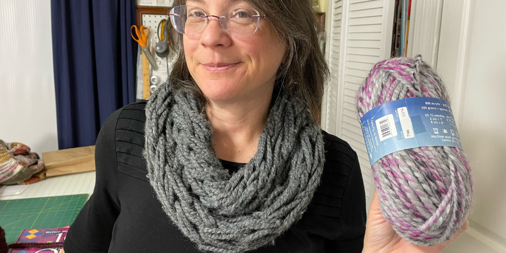 woman wearing arm knitted scarf and holding skein of yarn