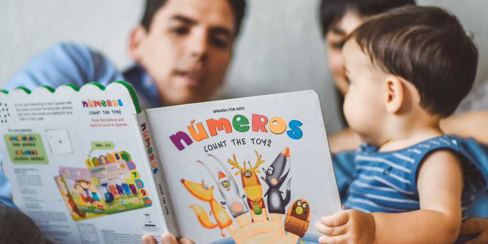 Parents with young child reading a book in Spanish