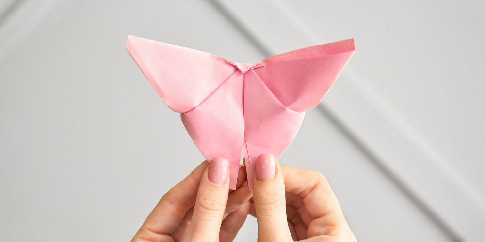 hands holding up pink origami butterfly