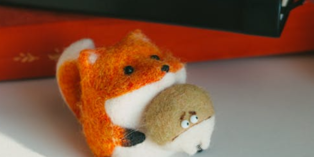 Felted fox holding another felted brown creature with a concerned expression